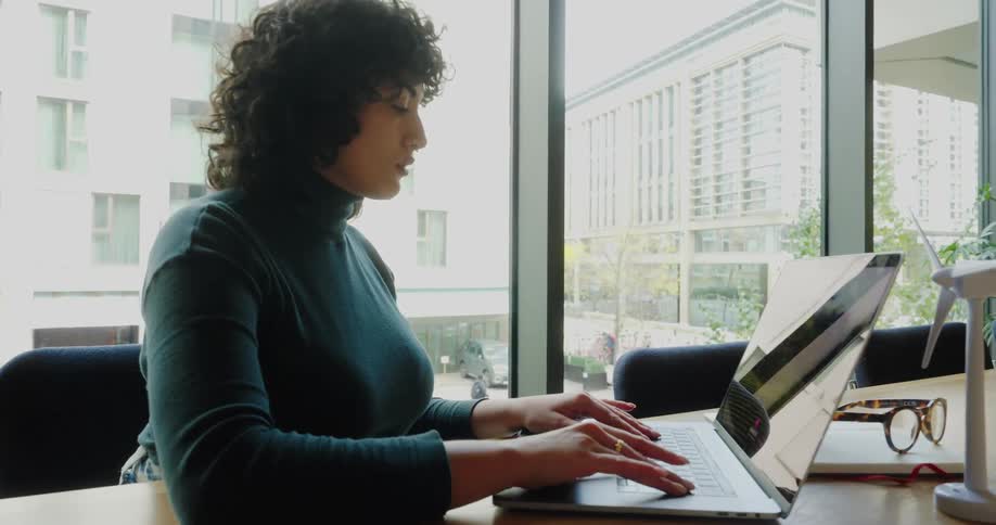 Woman sitting at an office desk opens the lid of her laptop computer and types on the keyboard