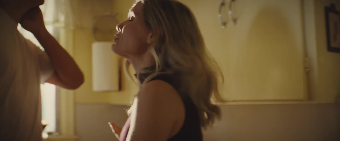 A young couple having a heated discussion in the kitchen with the young woman expressing her anger while the man stands across from her watching with a look of disappointment