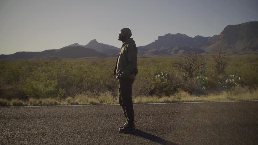 Man stands on a rural road with mountains in the distance as he looks behind him