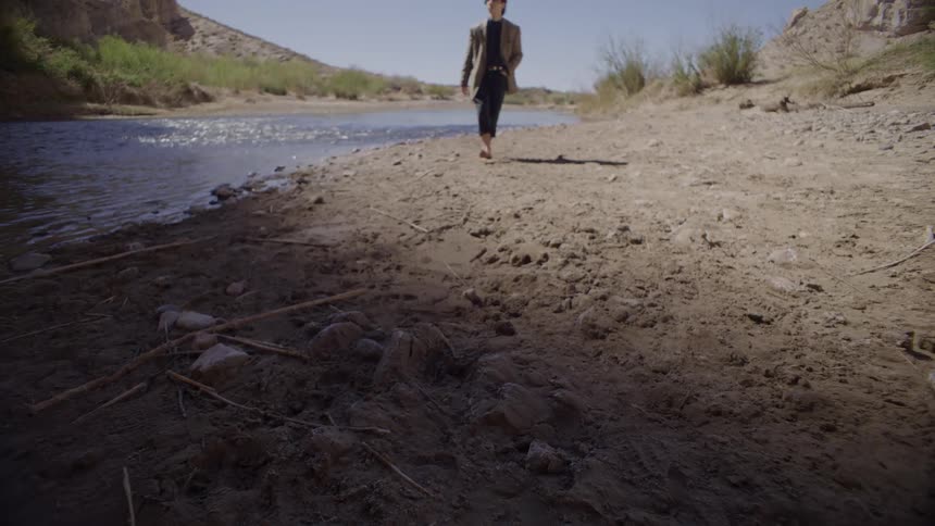 Young man walks barefoot along a flowing stream
