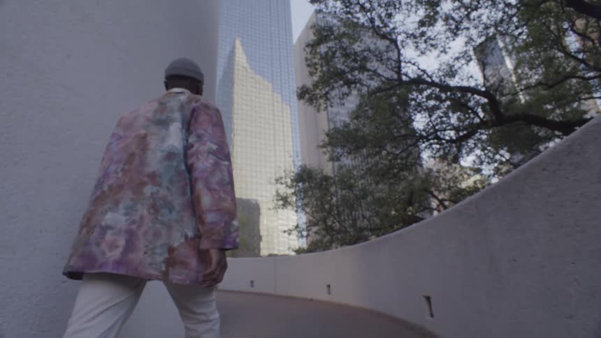 Man walks up the curving ramp of a building near a reflective skyscraper during the daytime
