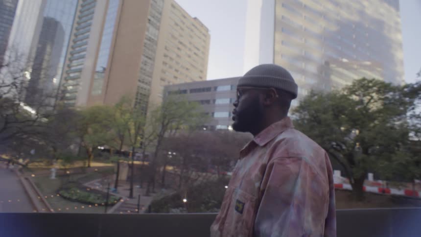 A black man is walking down a sidewalk ramp in a city with many skyscrapers and buildings