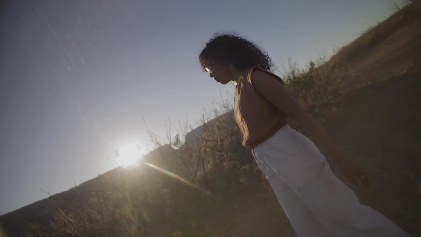 The woman walks past the tall grass as the sun rises