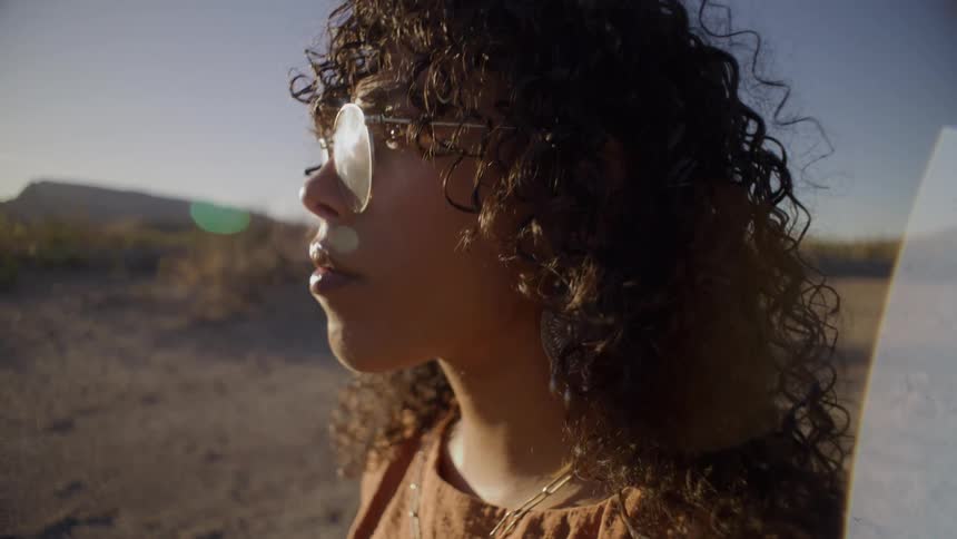 Curlyhaired woman with clear glasses in arid setting under golden light