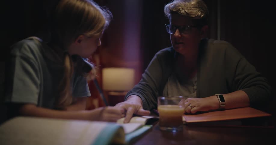 A mother helping her daughter with homework at the dining table with a glass of orange juice sitting nearby