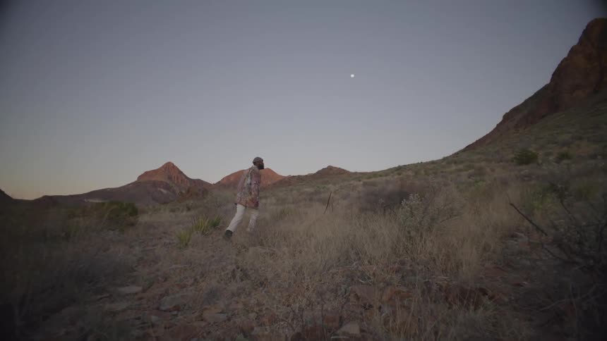 Man walks through dry grass on the side of a mountain