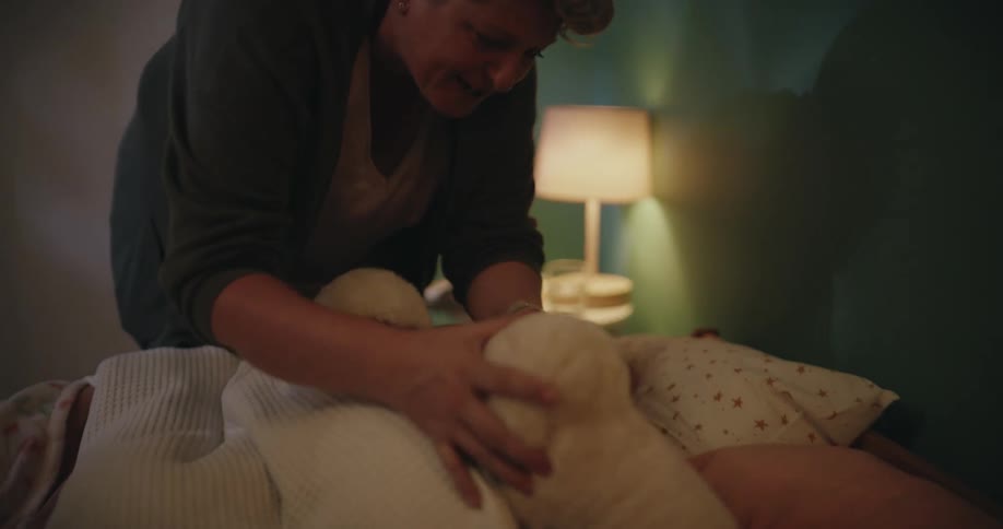 A mother kisses her young daughters goodnight while they lie in bed