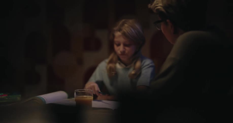 Little girl with a happy expression while doing a task accompanied by an adult at the table