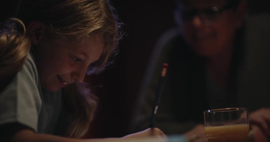 The grandmother talks with her granddaughter as she does homework