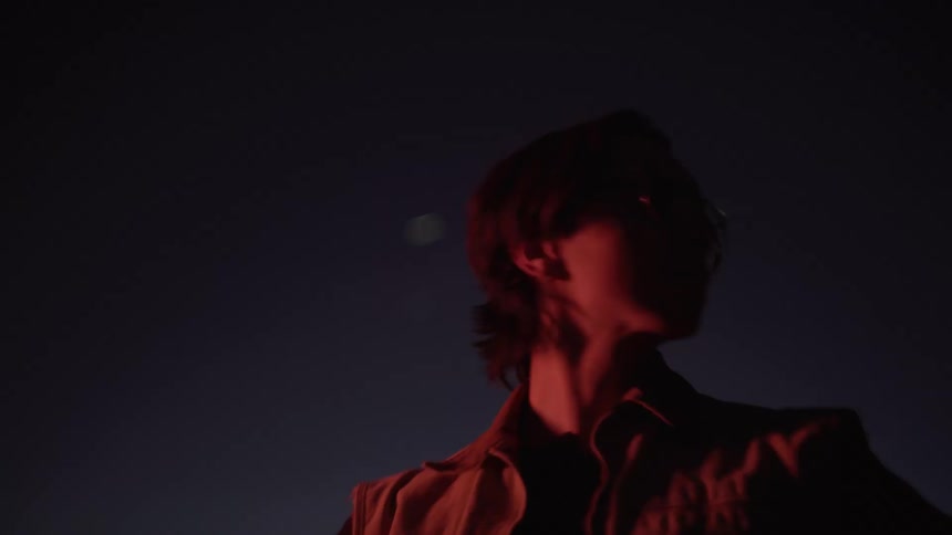 A man wearing a tan vest and glasses runs along a road at twilight before stopping to look up at the dark sky in a desert landscape