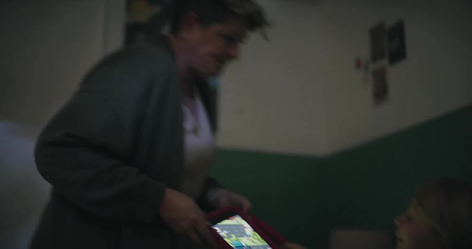 A young girl is using a tablet in bed at night when an adult enters the room and takes the device awayshe looks up in surprise and reaches out for the tablet before reluctantly settling back down to sleep