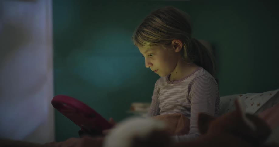 The girl is viewing her tablet in bed