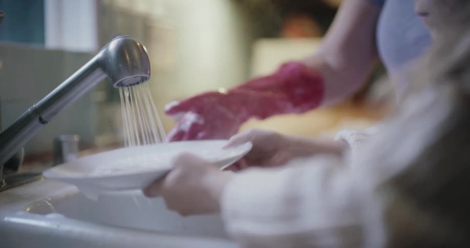 Child washes a plate in a sink with running water indoors