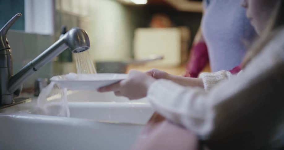 The mother and daughter run water over the dishes