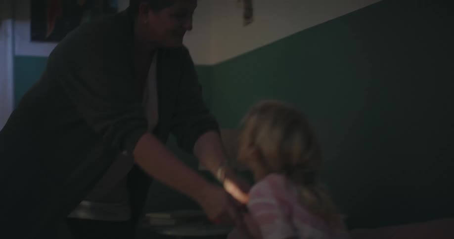 Male and female children playing in bed with a flashlight and an adult woman coming over and removing it from them indoors during night time