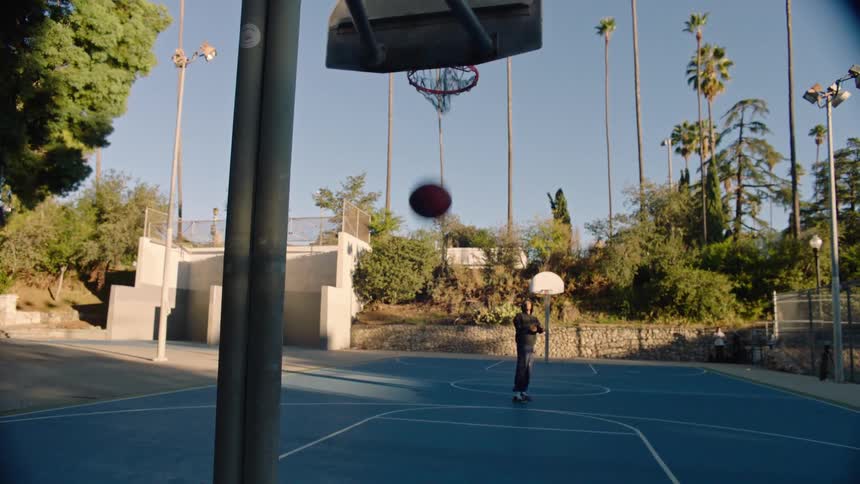 Young black male playing basketball and scoring a point in a basketball court outdoors during day time