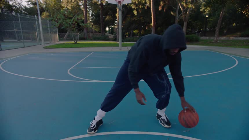 The man is dribbling the ball on the court outside