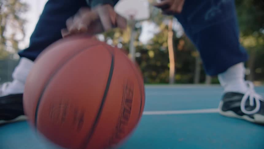 Black male hands dribbling a basketball at a basketball court in a park outdoors during dusk or dawn