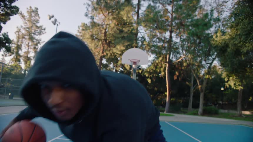 Young adult black man dribbling a basketball on a basketball court at a park outdoors during dusk or dawn