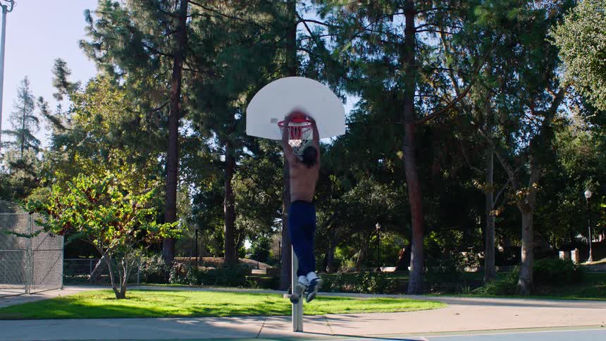 A black male athlete running with a basketball leaping and scoring a hoop during midday training while shirtless under bright sunlight