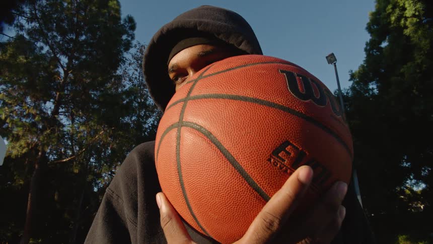 Young man wearing a hoodie stands outside holding a basketball