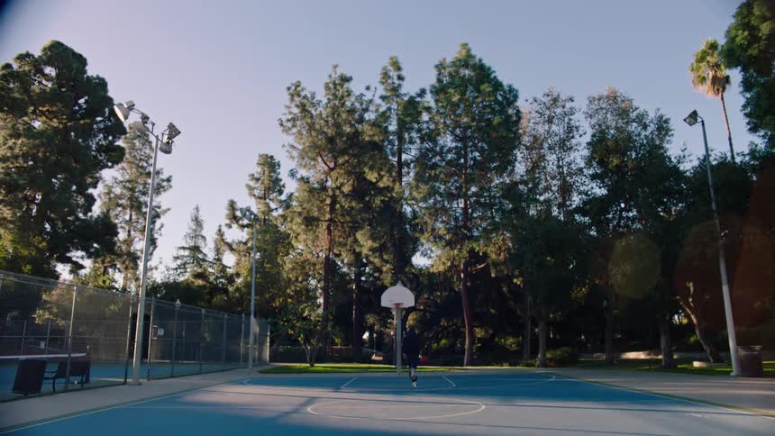 A person runs down an outdoor court while dribbling a basketball