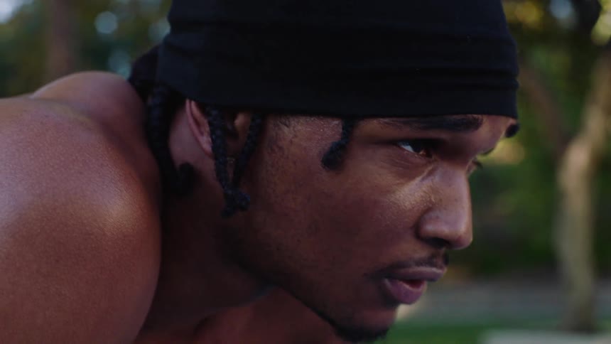 A black male athlete outdoors after a game bending forward to catch his breath