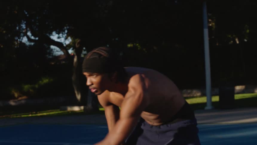 Young adult black man wearing a bandanna dribbling a basketball at a basketball court in a park outdoors