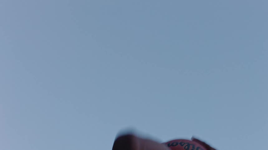 A man stretches his arm upward throwing a basketball against a clear blue sky in a low angle view