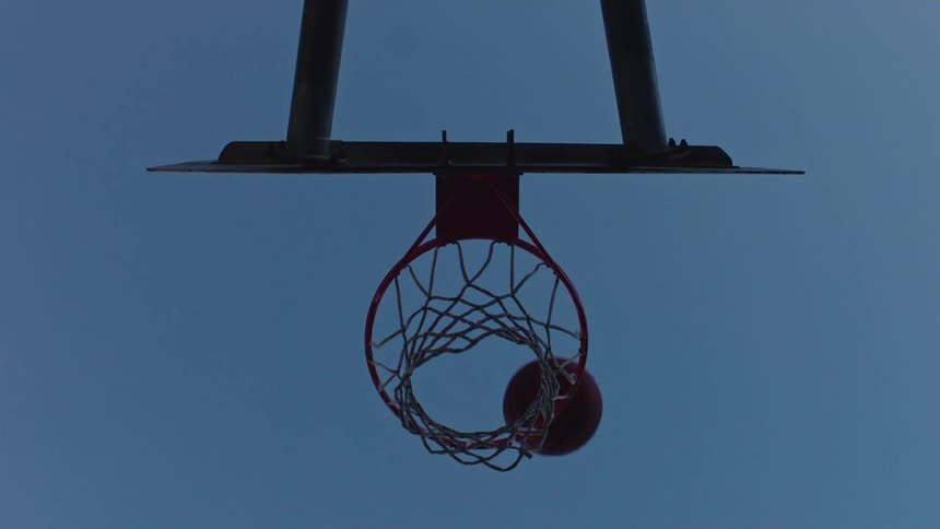 Basketball hits the basket seen from below against a clear blue sky
