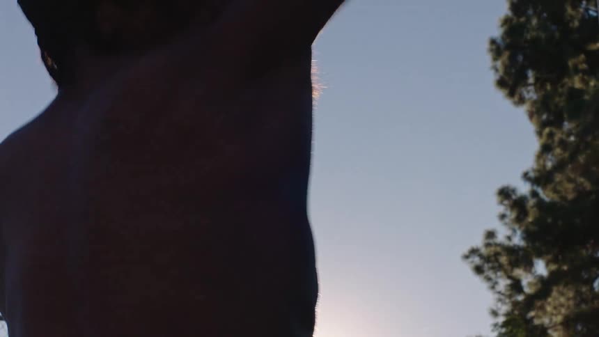 A young man on an outdoor basketball court at sunset throwing a basketball up toward the hoop as warm light fills the sky