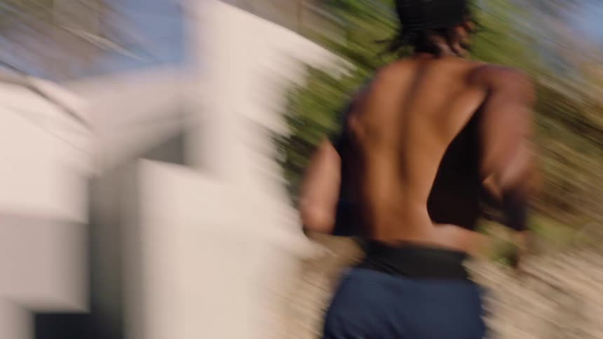 A young black man running shirtless across a basketball court on a bright sunny day