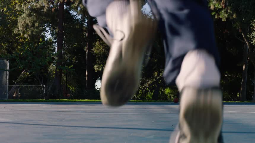 Shirtless young adult black man running on a sports courts and touching his hand to the floor before running more outdoors during day time