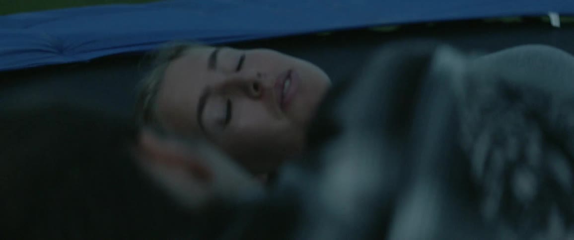 Two women laying on a trampoline outside talking and laughing