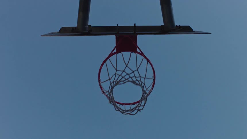 A male athlete dunking a basketball into the hoop during an outdoor game in the evening light