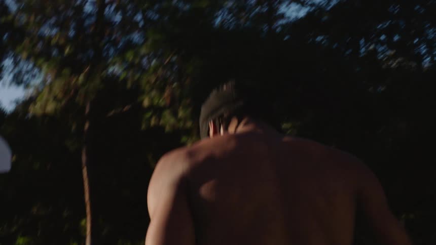 Person shoots a basketball on an outdoor court surrounded by trees