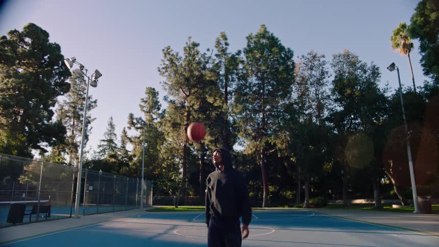A man wearing a black hoodie playing basketball in an outdoor court
