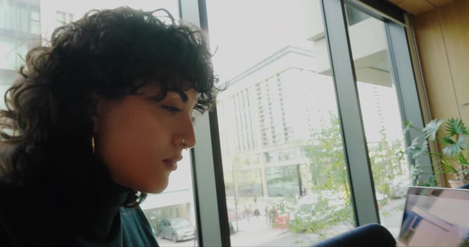 A young woman sits in an office while typing on a laptop computer
