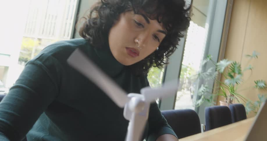 Woman sits at a table and handles a paper object while an open notebook rests nearby