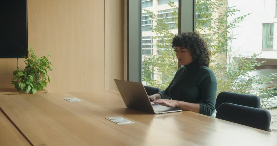 The woman sits down at the conference table and opens her laptop