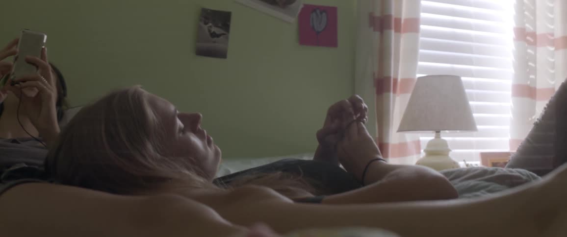 A woman plays with hair bands while leaning against another woman in bed