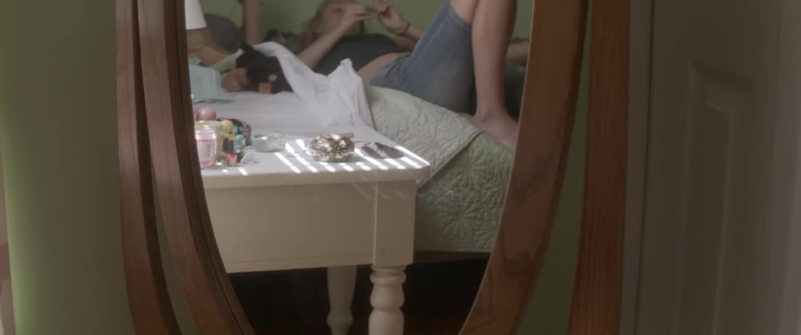 A mirror reflects two women laying in bed