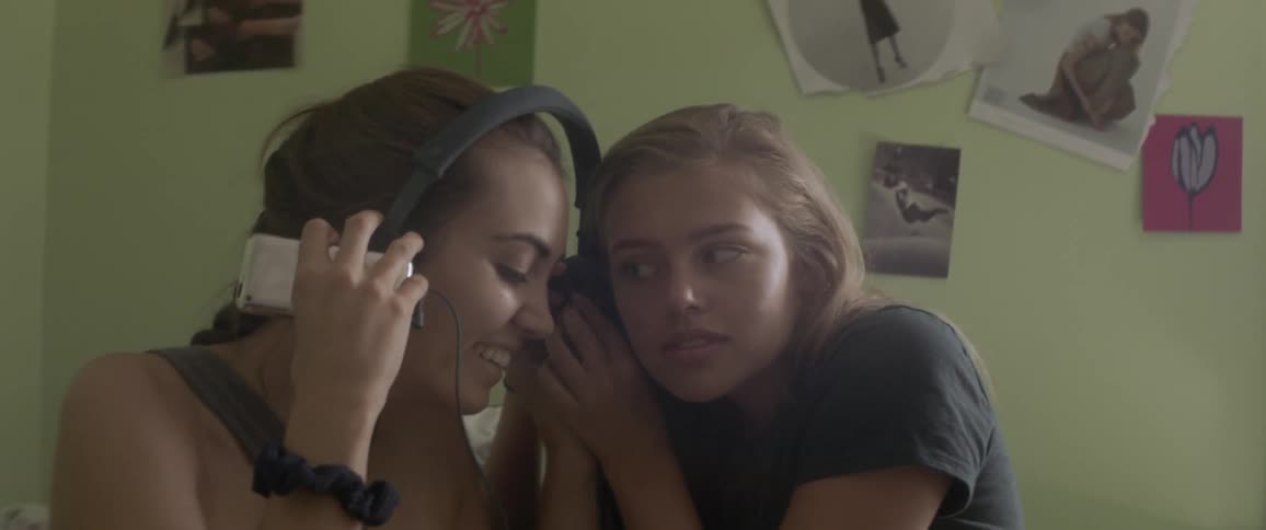 Two women sitting on a bed and listening to music with headphones