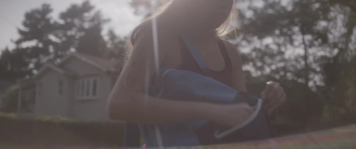 A woman walking in a neighborhood takes a pack of cigarettes out of a backpack
