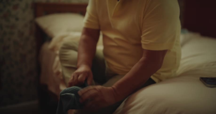 Close up of an asian man wearing his socks while sitting on a bed as he prepares to leave home