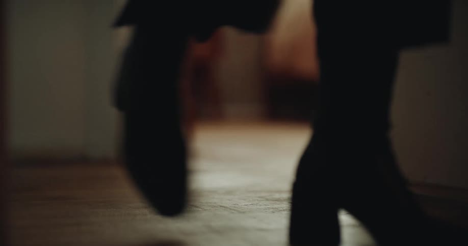 Two people walk on wooden floor wearing heeled boots in warmly lit indoor setting
