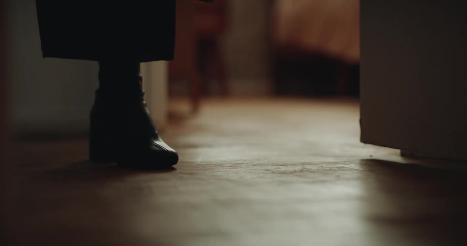 Black heeled boots worn on wooden floor in softly lit indoor setting