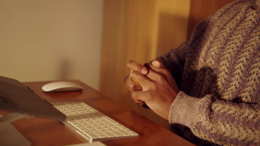 Person seated at desk with hands clasped in front of white keyboard and wireless mouse