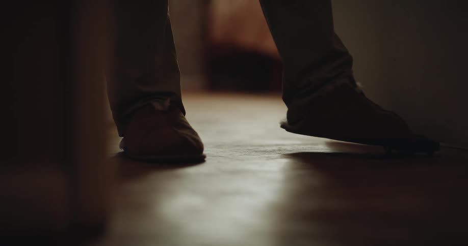 A person in pajamas walking through the living room accidentally kicking a toy car that slides under the couch