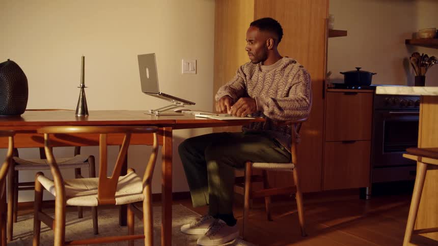 Man sitting at a table with a laptop computer opens his notebook and begins to type on the keyboard